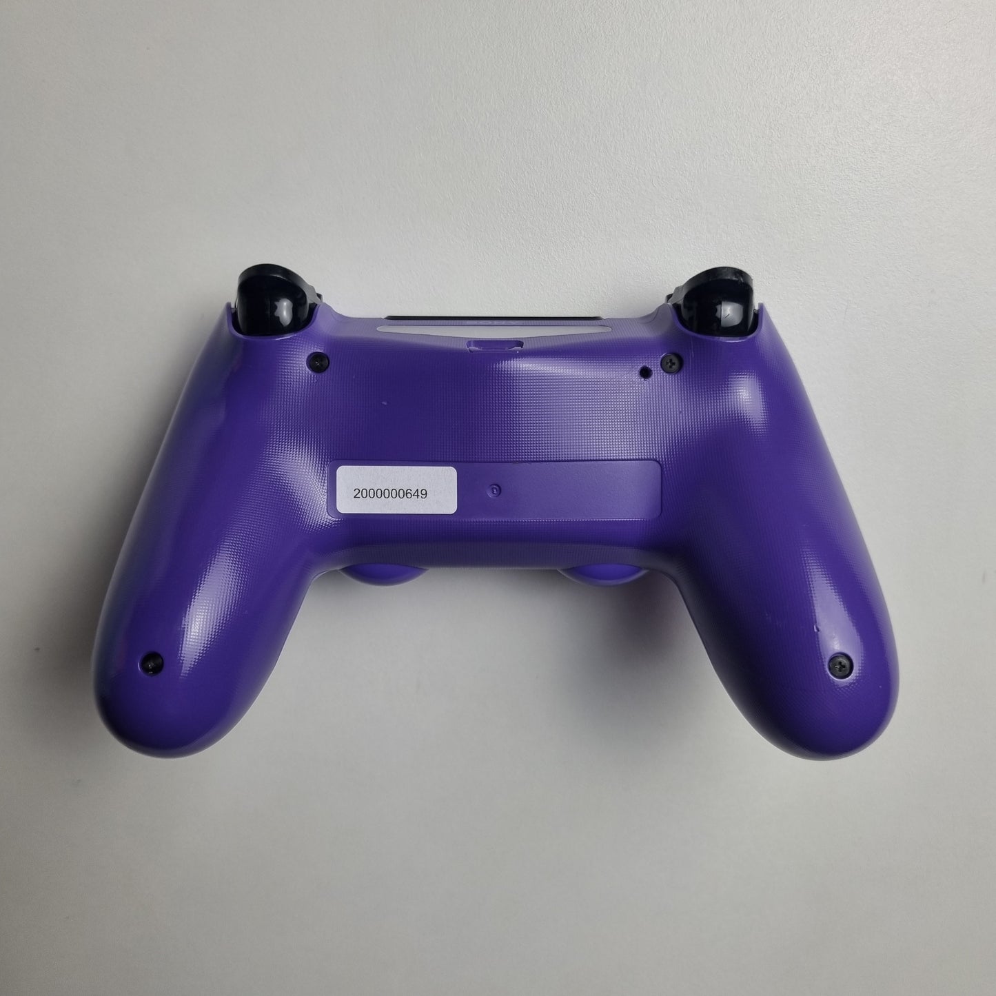 Back of an electric purple official Sony PlayStation DualShock 4 refurbished gaming controller on a light gray background