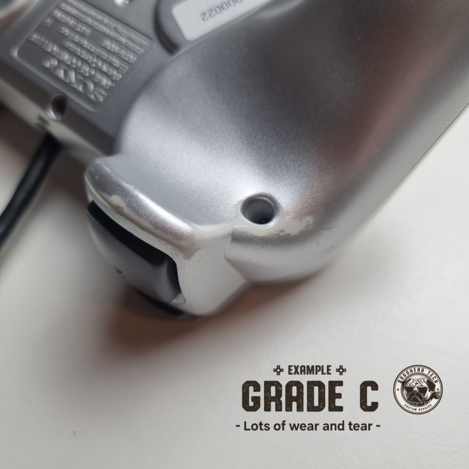Close-up of some wear and tear on a refurbished official silver Sony PlayStation 2 wired controller, with the caption 'Grade C: Lots of wear and tear' in the bottom corner.